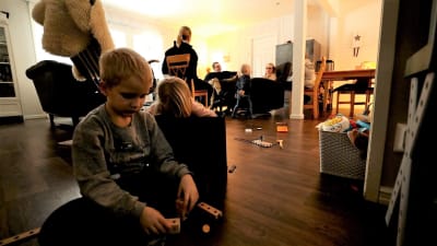 Barn som leker på golvet. Vuxna sitter i bakgrunden.