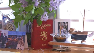 Ett skrivbord med fotografier på biskopar, en vas med syrener och en röd bok med Finlands lag 2013.