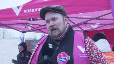Ralf Björklund framför Vänsterförbundets kampanjstånd och iklädd partiets ljusröda signalväst.
