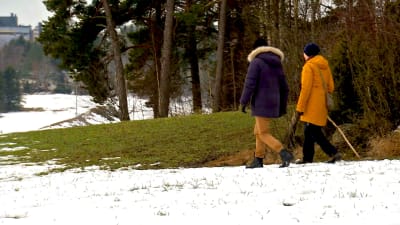 Två personer som går längs med en gräsplan. Snö på marken. 