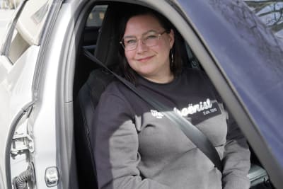 En kvinna med svart tröja och ljusa glasögon sitter i en bil och tittar ut.