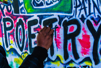 Käsi maalaamassa poetry -graffitia seinään.