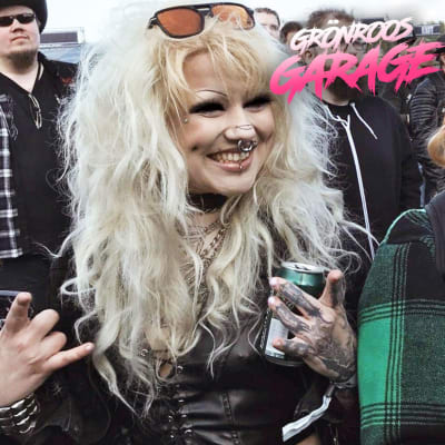 Kvinna med tatueringar och ölburk gör horntecken på festival.