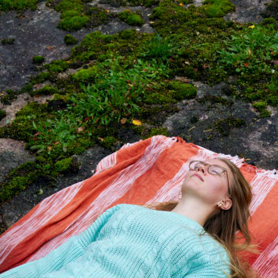Nainen makaa punaisella viltillä kalliolla
