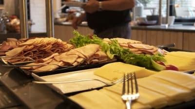 Ett buffébord med frukostprodukter, såsom ostar, skinkor och pålägg.