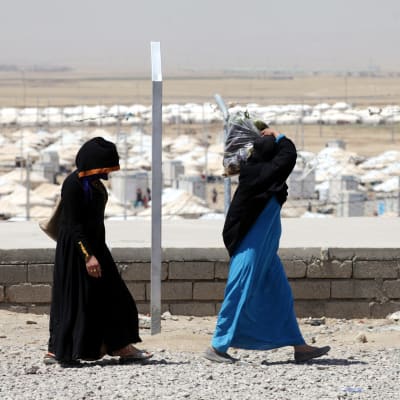 Två kvinnor går utanför ett flyktingläger i Irak.