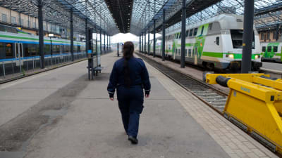En kvinna i blå uniform promenerar på en tom tågperrong.