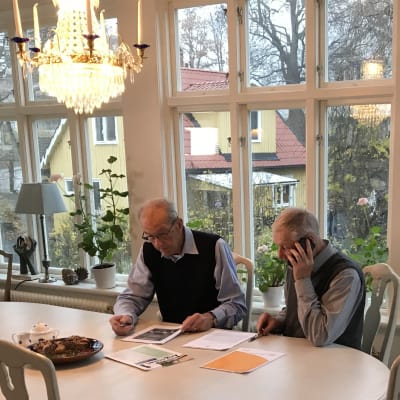 Karl-Olof Fagerström och Ingemar Wemmenhög från Waxholmspartiet sitter vid ett bord i en glasveranda med papper framför sig.