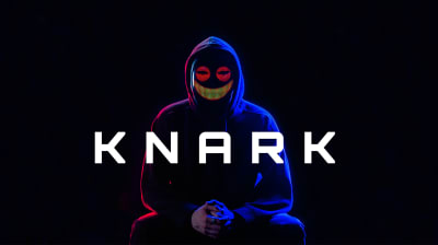 En person klädd i en svart munkjacka sitter. Personen är anonymiserad med en LED-mask. På LED-masken ses ett skrämmande ansikte med stora röda ögon och ett brett gult leende.