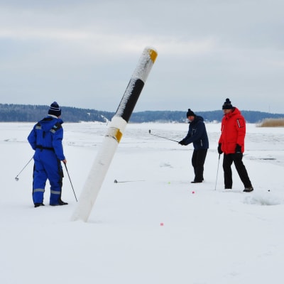 Fem herrar står på isen bredvid ett sjömärke och spelar golf.