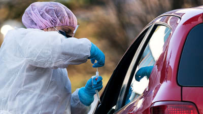 En anställd vid vårdbolaget Mehiläinen testar en patient för coronaviruset så att patienten sitter i sin bil.