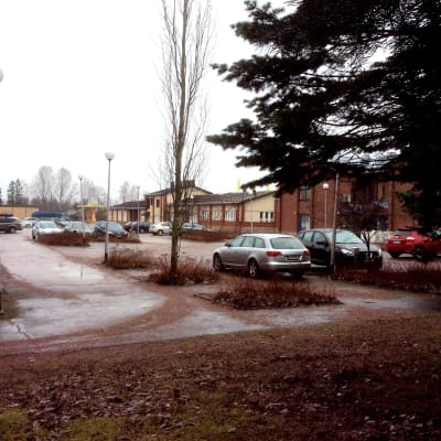 Bilar parkerade vid kommungården i Sjudenå. Affärer och andra hus syns också.