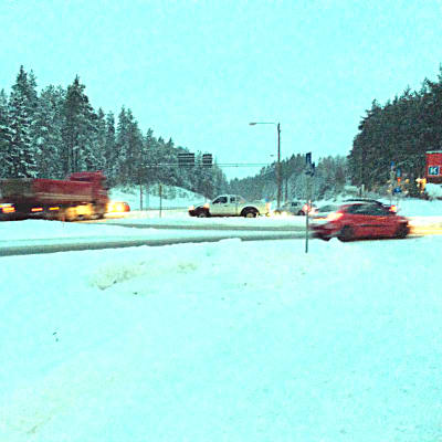 En landsvägskorsning och snöigt landskap. Långtradare och bilar kör i olika riktningar. Vägen ser hal ut. Det är skymning.