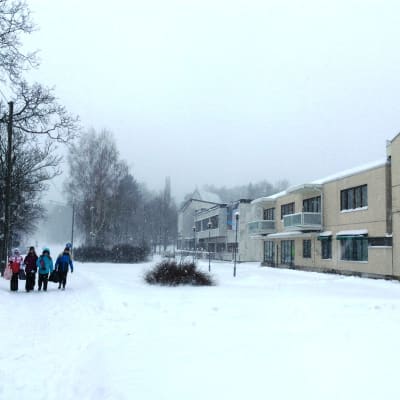 Barn går på en snöig gångled, kontors- och affärshus till höger, en stenkyrka skymtar i bakgrunden.