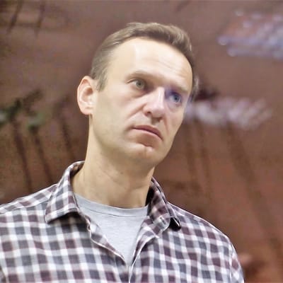 Aleksei Navalnyi seisoo ruutupaidassa lasikopissa oikeussalissa.