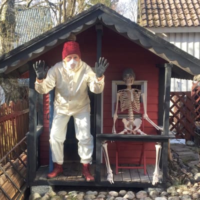 Kvinna i skyddsutrustning och ett skelett framför en lekstuga.