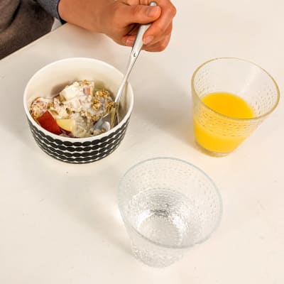 Aamiaispöydällä kipossa omenaa, mysliä ja jugurttia. Lasi vettä ja lasi appelsiinimehua.