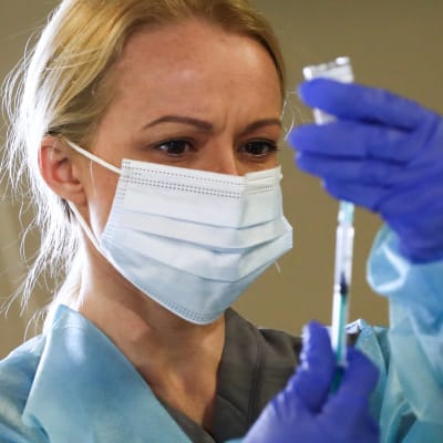 En sjukskötare i munskydd håller upp en spruta.