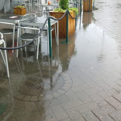Översvämmad dagvattenbrunn vid café.