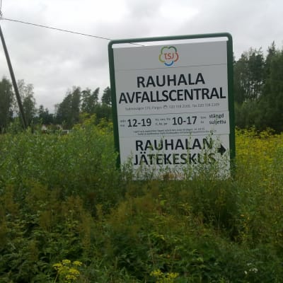 Skylt i högt gräs som berättar vilka tider Rauhala avfallscentral i Pargas har öppet.