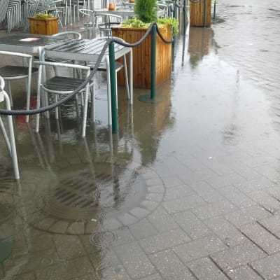 Översvämmad dagvattenbrunn vid café.