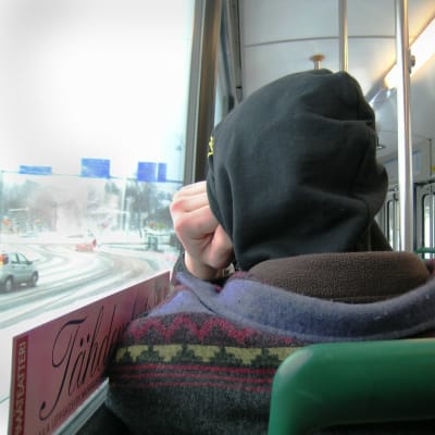 En person sitter i en buss, ryggen vänd mot kameran. 