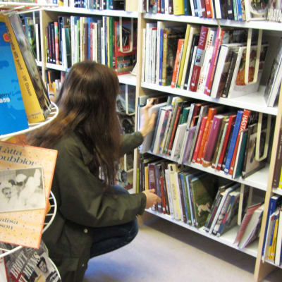 En kvinna sitter på huk vid en hylla med böcker på ett bibliotek.