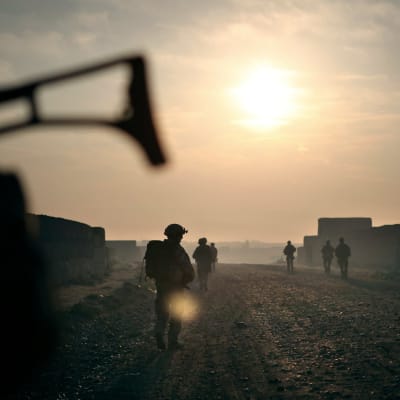 Sotilaat etenevät parijonossa hiekkatiellä kellertävää aurinkoa vasten kuvattuna.