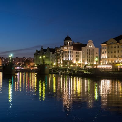 Kaliningrads stadsbyggnader som lyses upp av lampor på natten vid floden. 