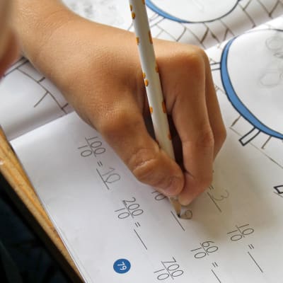 Närbild på en elevs hand som skriver i matematikboken.