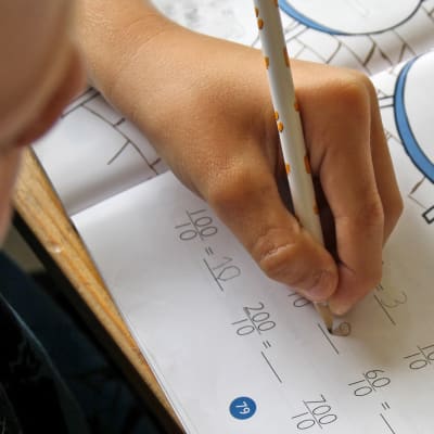 Närbild på en elevs hand som skriver i matematikboken.