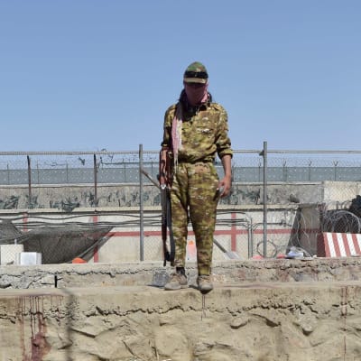 En talibankrigare övervakar platsen där bombdådet utanför Kabuls flygplats inträffade.