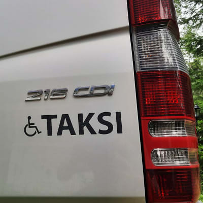 Rullstolssymbol och ordet Taksi i bakändan på en stor taxibil.