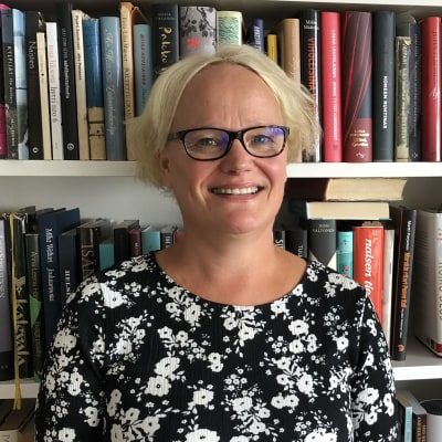 En blond kvinna står framför en bokhylla.