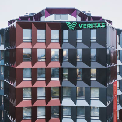 Ett hus med röda och blåa fönster. På taket en grön skylt med texten Veritas.