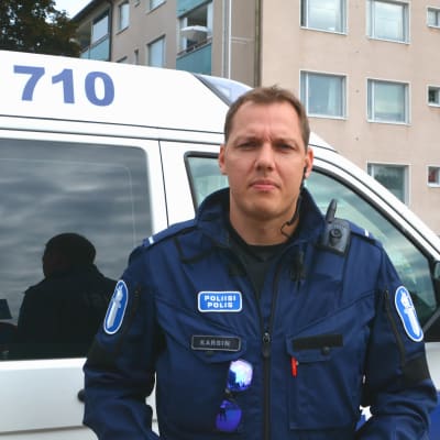 Man i polisuniform står framför polisbil.