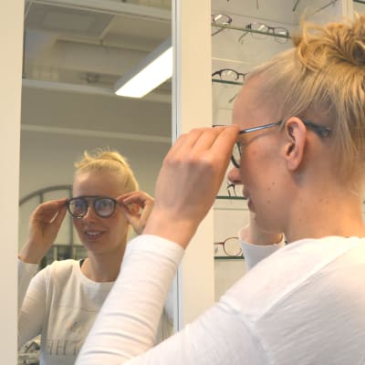 Kvinna provar glasögon framför spegel.