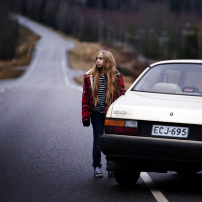 Tolvåriga Varpu står ensam på en landsväg utanför en övergiven bil.
