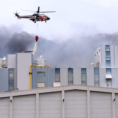 Rajavartiolaitoksen helikopteri tiputtaa vettä tehtaaseen.