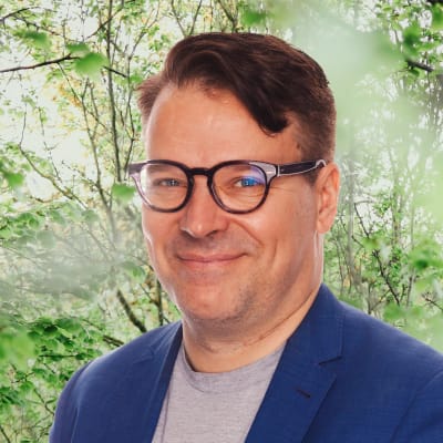 Ville Niinistö ler mot kameran. I bakgrunden syns grönskande buskage.
