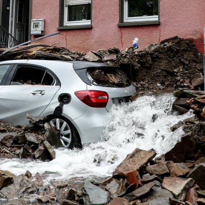 Bil som är täckt av byggmassor efter en storm. Vatten strömmar ut vid bilen