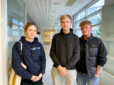 Tre gymnasiestuderande står i en korridor.