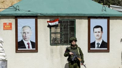 En rysk militärpolis, står mellan porträtt av Rysslands president och Syriens president, vid en vägspärr i Wafidiin. Vägspärren finns i utkanterna av Damaskus på vägen mot östra Ghouta. 