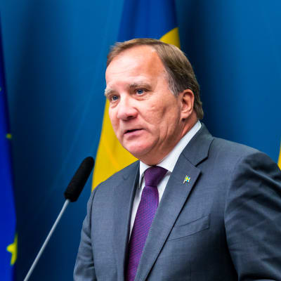 Stefan Löfven på pressträff framför EU-flagga och flera Sverigeflaggor.
