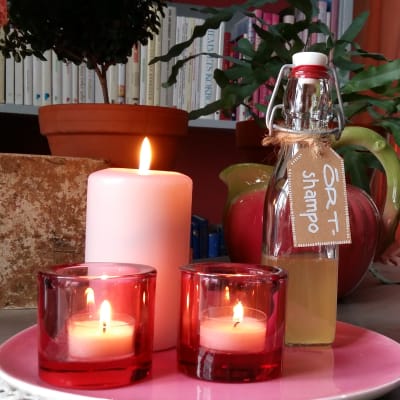 En flaska hemgjord örtshampo på ett bord med tända ljus.
