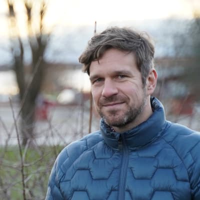 En leedne mörkhårig man i mörkblå jacka, fotad ute.