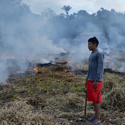 En man står vid en område som brinner i en by i Brasilien.