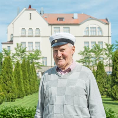 Kevään 2018 vanhin ylioppilas Matti Dahlbacka hymyilee Pietarsaaren lukion edessä ylioppilaslakki päässään.
