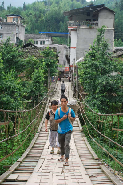 En man och en kvinna med korgar på ryggen går på en gångbro.