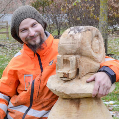 Niko Nordström ler och har armen runt en skulptur av en snigel som sitter på en sopp.